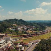 Vista aérea de uma pequena cidade entre morros verdes, atravessada por linhas ferroviárias.