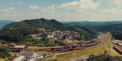 Vista aérea de uma pequena cidade entre morros verdes, atravessada por linhas ferroviárias.