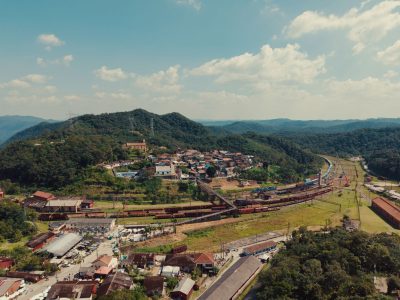 Vista aérea de uma pequena cidade entre morros verdes, atravessada por linhas ferroviárias.