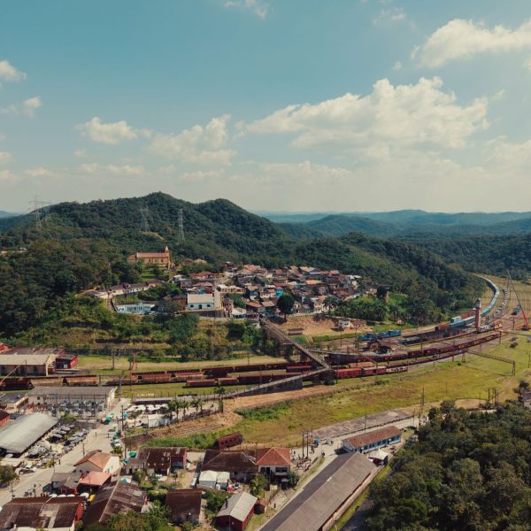 Vista aérea de uma pequena cidade entre morros verdes, atravessada por linhas ferroviárias.
