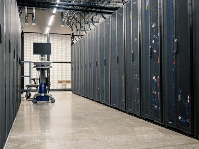 Armários metálicos com servidores, dispositivos de rede e cabos no interior de um data center moderno.