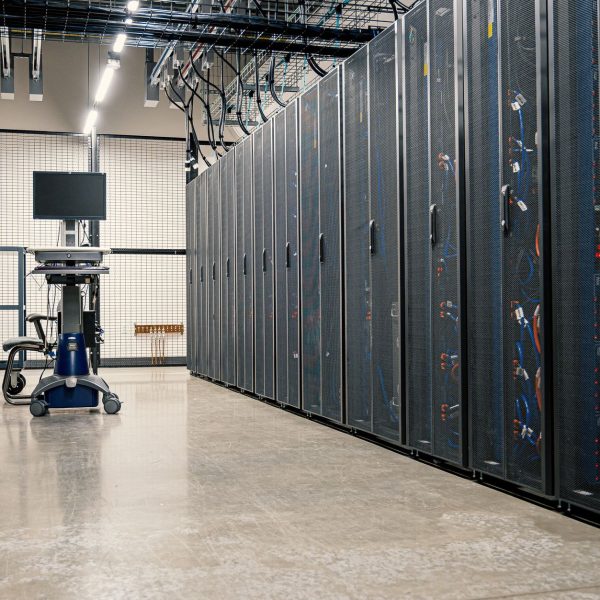 Armários metálicos com servidores, dispositivos de rede e cabos no interior de um data center moderno.