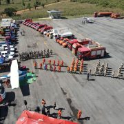 Vista aérea de caminhões, veículos de emergência e equipes reunidos durante um exercício de treinamento.