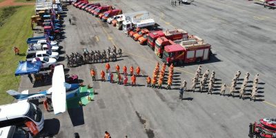 Vista aérea de caminhões, veículos de emergência e equipes reunidos durante um exercício de treinamento.