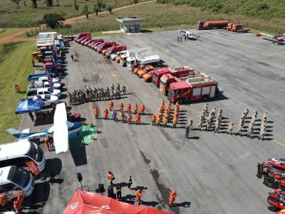 Vista aérea de caminhões, veículos de emergência e equipes reunidos durante um exercício de treinamento.