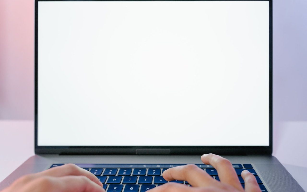 Mãos digitando em um laptop com a tela em branco