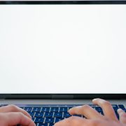 Mãos digitando em um laptop com a tela em branco