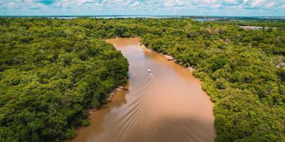 Vista aérea de uma embarcação navegando por um rio barrento cercado pela floresta amazônica.