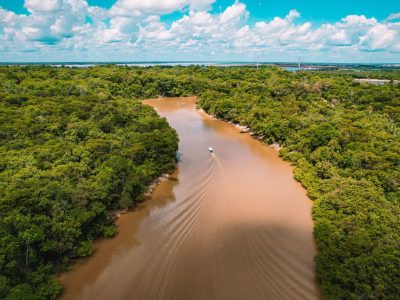 Vista aérea de uma embarcação navegando por um rio barrento cercado pela floresta amazônica.