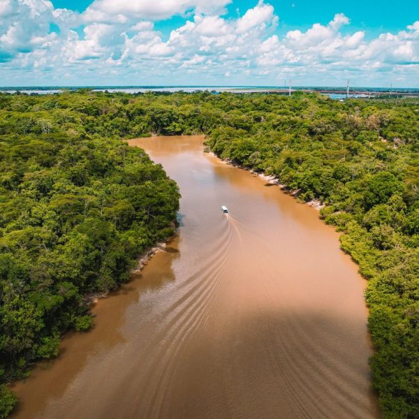 Vista aérea de uma embarcação navegando por um rio barrento cercado pela floresta amazônica.
