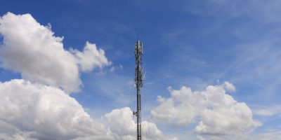 Torre de comunicação contra um céu azul com nuvens brancas.