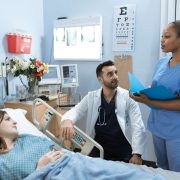 Médicos e enfermeira discutem o tratamento de um paciente em um quarto de hospital.