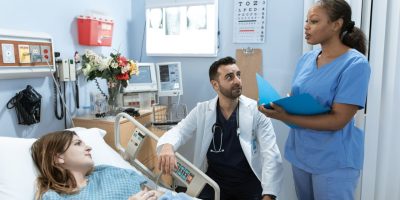 Médicos e enfermeira discutem o tratamento de um paciente em um quarto de hospital.