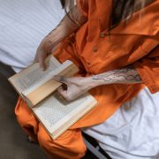 Mulher privada de liberdade lê um livro sentada em uma cama dentro de uma cela.