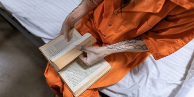Mulher privada de liberdade lê um livro sentada em uma cama dentro de uma cela.