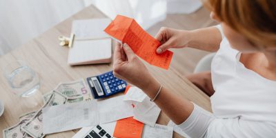 Mulher usa uma calculadora e analisa recibos em uma mesa para organizar as finanças domésticas.
