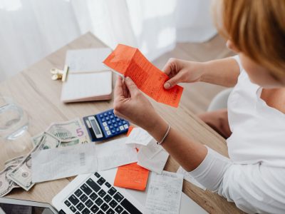 Mulher usa uma calculadora e analisa recibos em uma mesa para organizar as finanças domésticas.