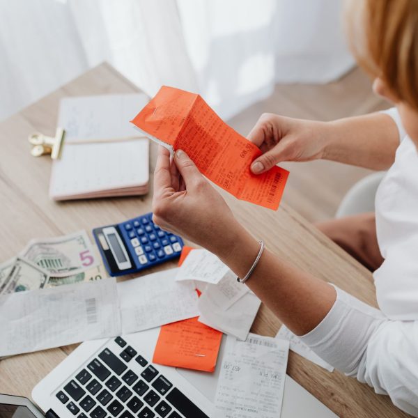 Mulher usa uma calculadora e analisa recibos em uma mesa para organizar as finanças domésticas.